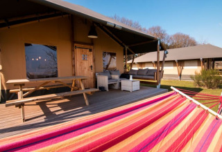 Veranda van 'De Lodge' met picknicktafel, hangmat en zitruimte bij Glamping de Bosweide in Nederland.