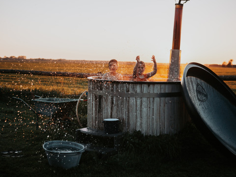 Twee kinderen spelen en spetteren in een buitenbad met zonsondergang en landelijke velden op de achtergrond.