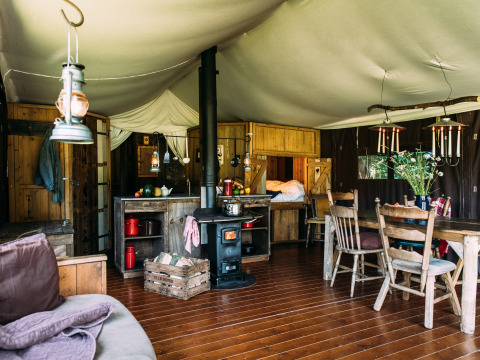 Alojamiento glamping acogedor con muebles de madera, estufa, mesa de comedor y cama en parque vacacional.