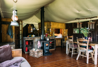 Cozy glamping accommodation with wooden furniture, wood stove, dining table, and sleeping area in holiday park.