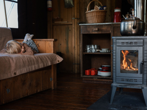 Gemütlicher Innenraum mit Kind auf Sofa und brennendem Holzofen in einer Glamping-Unterkunft.