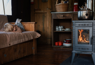 Knus interieur met een kind op de sofa en een houtkachel aan in een glampingverblijf.