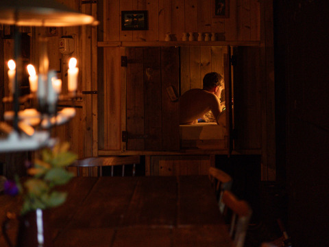 Un uomo si rilassa in una baita di legno illuminata da candele in un'accogliente struttura di glamping.