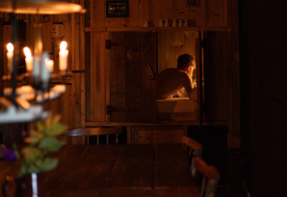 A man relaxes in a wooden cabin with candlelight ambiance at a cozy glamping holiday park accommodation.