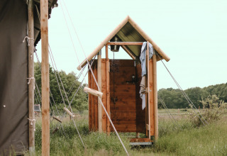 Wooden outdoor shower at a glamping site, surrounded by tents and greenery in a natural open setting.