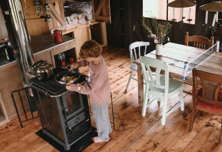 Een kind kookt op een fornuis in een gezellige glampinghut met houten vloer en een tafel vlakbij.