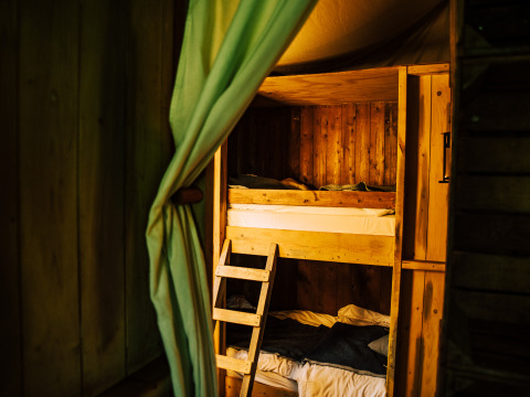 Wooden bunk beds with green curtain in a glamping tent at a holiday park, cozy and rustic atmosphere.
