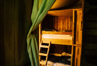 Wooden bunk beds with green curtain in a glamping tent at a holiday park, cozy and rustic atmosphere.
