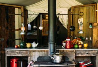 Rustic glamping kitchen with wood counters, fresh vegetables, lanterns, and cookware in a holiday park.