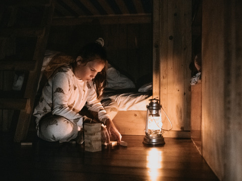 Bambina in pigiama gioca con blocchi di legno accanto a una lanterna in una cabina glamping di sera