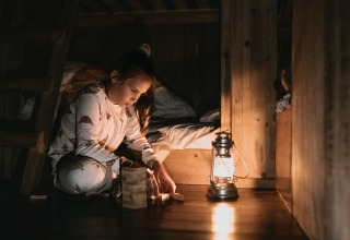 Child in pajamas playing with wooden blocks by a lantern at night in a cozy glamping cabin at holiday park