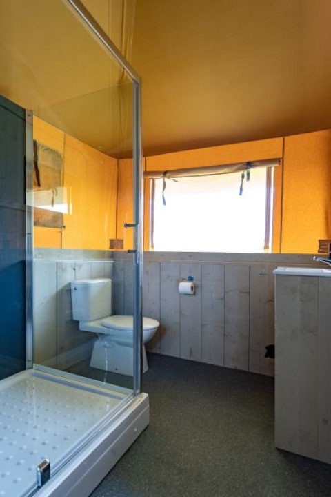 Badkamer in safaritent 'De Medley' met douche, toilet en raam bij Glamping de Bosweide in Nederland.