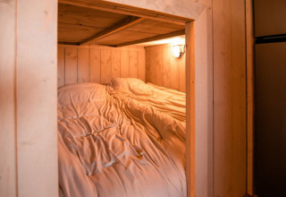 Gezellige slaapruimte met houten wanden en sfeerverlichting in een safaritent bij Glamping de Bosweide.