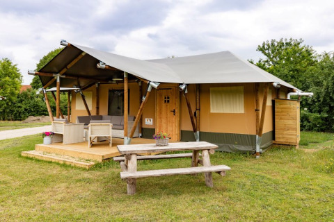 Safaritent De Medley met houten terras, buitenzitje en picknicktafel op een grasveld, overdag genomen.