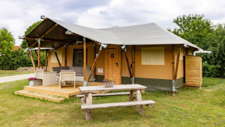 Safari-teltet De Medley med træterrasse, udelivsmøbler og bænk i grønne omgivelser, taget om dagen.