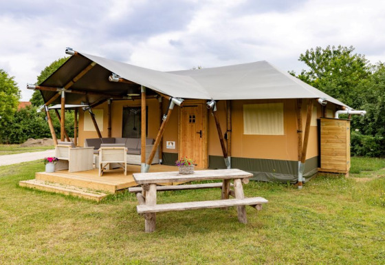 Safaritent De Medley met houten terras, buitenzitje en picknicktafel op een grasveld, overdag genomen.
