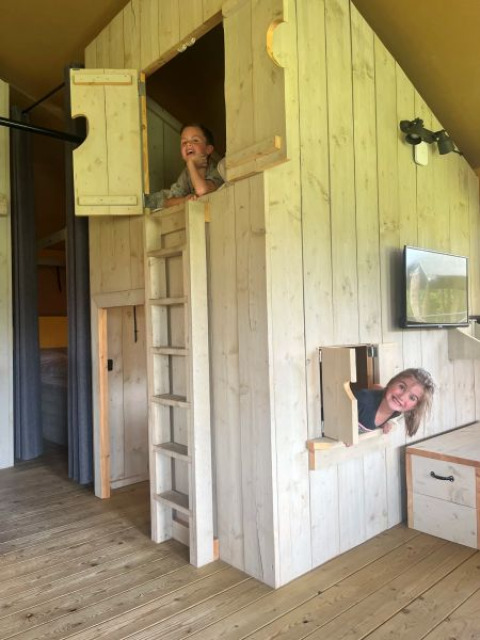To børn leger i en hytte med trævægge og små vinduer i en safaritelt ved Glamping de Bosweide, Holland.