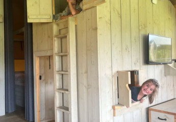 Zwei Kinder spielen in einem hölzernen Spielhaus in einem Safarizelt bei Glamping de Bosweide, Niederlande.