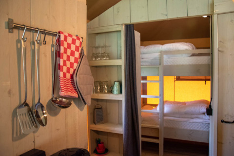 Interior de una tienda safari con utensilios de cocina, literas y estanterías en Glamping de Bosweide, Países Bajos.