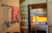 Interno di una tenda safari con utensili da cucina, letti a castello e scaffali a Glamping de Bosweide, Paesi Bassi.