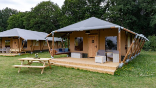 Tenda safari moderna con veranda in legno, area salotto esterna e tavolo da picnic in mezzo al verde.