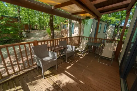 Overdekt houten terras met tuinmeubilair bij Cube Suite in Chianti Glamping Resort, Italië, omgeven door bomen.