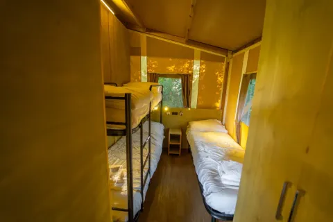 Gemütliches Schlafzimmer mit Etagenbetten und Einzelbetten im Lodge Tent Deluxe des Chianti Glamping Resort, Italien.