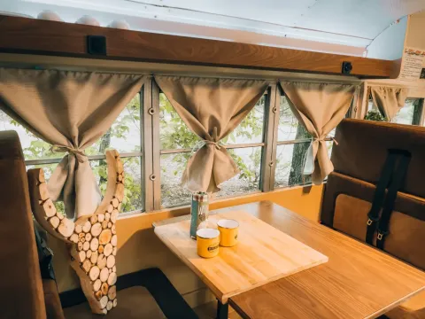Intérieur d’une tiny house bus scolaire au Chianti Glamping Resort, avec table, tasses et fenêtres décorées.