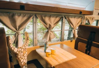 Intérieur d’une tiny house bus scolaire au Chianti Glamping Resort, avec table, tasses et fenêtres décorées.
