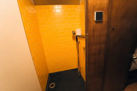 Douche dans une tiny house 'Schoolbus' au Chianti Glamping Resort, murs carrelés jaunes et porte en bois.