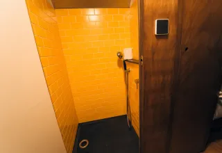 Douche dans une tiny house 'Schoolbus' au Chianti Glamping Resort, murs carrelés jaunes et porte en bois.