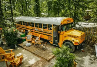 Un bus scolaire jaune transformé en tiny house avec terrasse en bois dans la forêt du Chianti Glamping Resort, Italie.