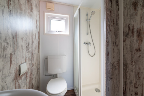 Pequeño baño en Forest lodge del camping Veluwe De Pampel con ducha, inodoro y ventana.
