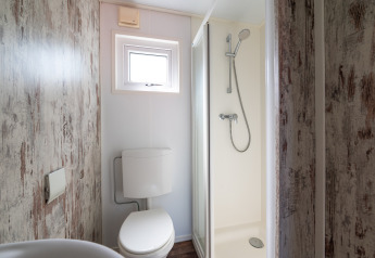 Compact bathroom inside Forest lodge at Veluwe campsite De Pampel, featuring shower, toilet and window.