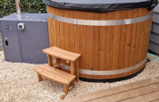 Bañera de hidromasaje exterior de madera con tapa negra y escalera en Veluwelodge XL, De Boshoek, Países Bajos.