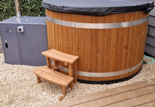 Wooden outdoor hot tub with black cover and steps near Veluwelodge XL at De Boshoek recreation park, Netherlands.