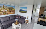 Sala de estar en una casa flotante en Marina Parcs Ámsterdam con sofá gris, cocina y cuadros en la pared.