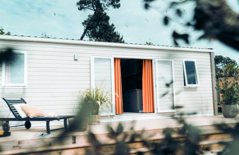 Timber Lodge met terras, oranje gordijnen en ligstoel bij Eurocamping Vessem BV in Nederland.
