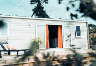 Timber Lodge avec terrasse en bois et rideaux orange à Eurocamping Vessem BV, Pays-Bas, entouré de verdure.