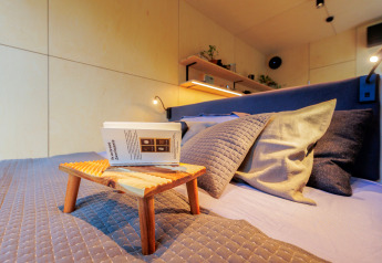 Moderne soveværelsesinteriør i et tiny house med hylde, puder, plaid og lille træbord med bog.