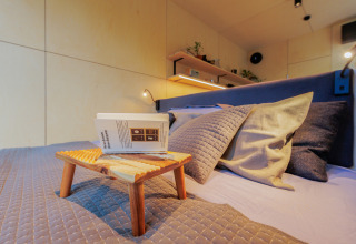 Gemütliches Schlafzimmer in einem Tiny House mit Holzregalen, Kissen und einem kleinen Tisch mit Buch.