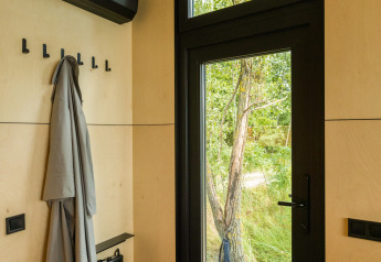 Modern entryway of tiny house with glass door, coat rack, and nature outside at Holiday park Eigen Wijze.