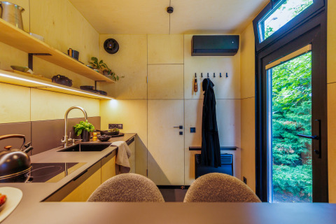 Moderne Küchen- und Eingangsbereich in einem Tiny House mit großen Fenstern und Blick ins Grüne.