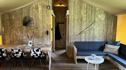 Interior de tienda safari de lujo con paredes de madera, comedor y sala en Outdoor Centre Hessenheem.