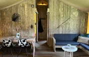 Interior de tienda safari de lujo con paredes de madera, comedor y sala en Outdoor Centre Hessenheem.