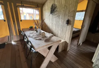 Interior view of a luxury safari tent with wooden dining table at Outdoor Centre Hessenheem, Netherlands.