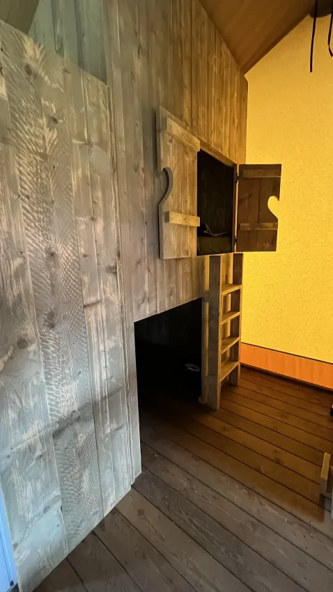 Interieur van een luxe safaritent bij Outdoor Centre Hessenheem, Nederland, met houten muren en een loft.