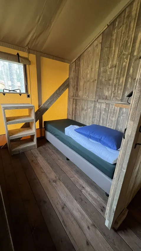 Interior de una tienda safari de lujo en Outdoor Centre Hessenheem, Países Bajos, con cama y estante.