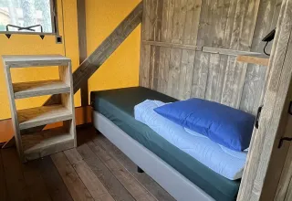 Interior de una tienda safari de lujo en Outdoor Centre Hessenheem, Países Bajos, con cama y estante.