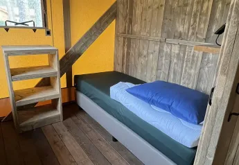 Interior de una tienda safari de lujo en Outdoor Centre Hessenheem, Países Bajos, con cama y estante.